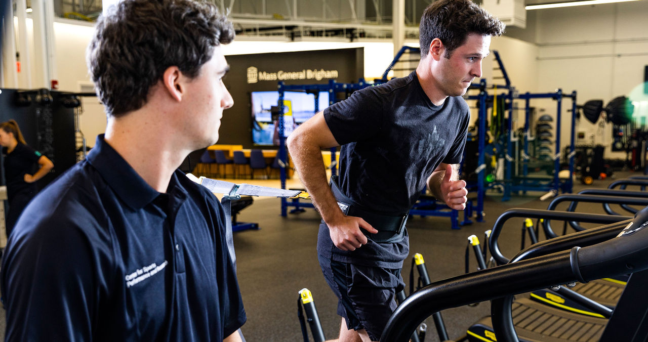 male trainer supervising a male athlete on running equipment in gym