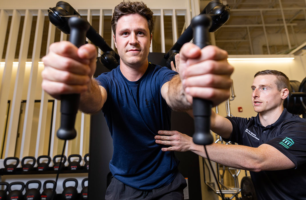  man using weight machine supervised by trainer in gym
