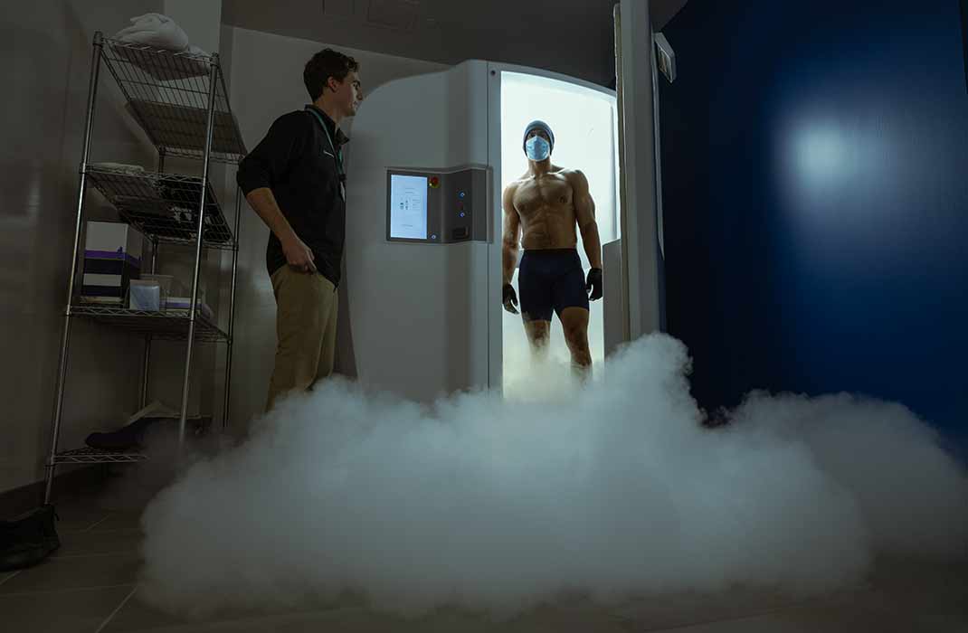 male athlete standing in cryo therapy chamber with staff member 