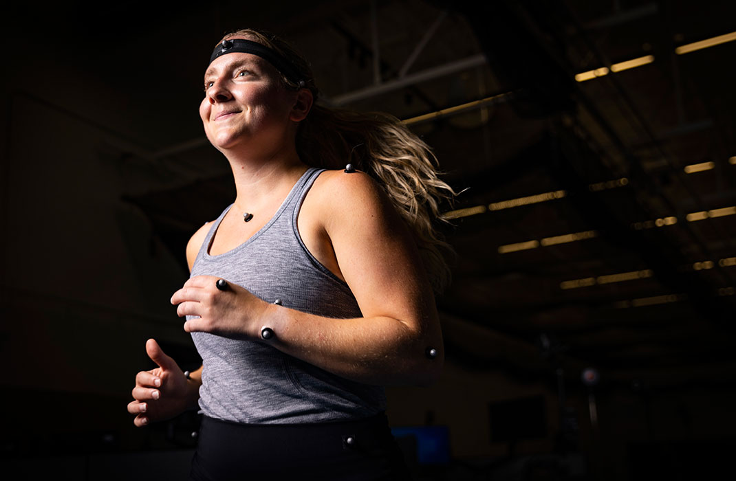female athlete running in gym with nodes attached on her arms, head and chest