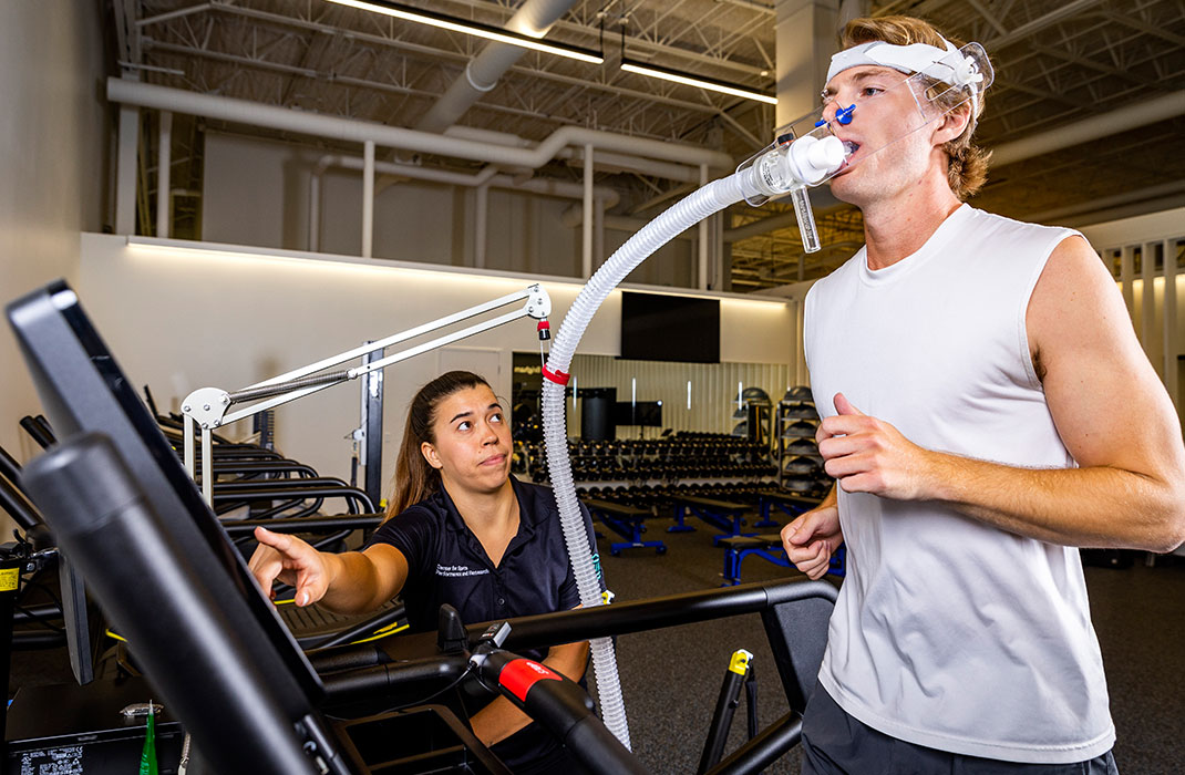 female trainer supervising male athlete on treadmill with oxygen machine attached on face
