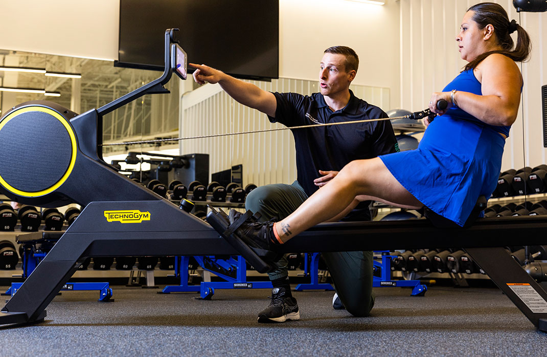 woman on a rowing machine in gym supervised by male trainer