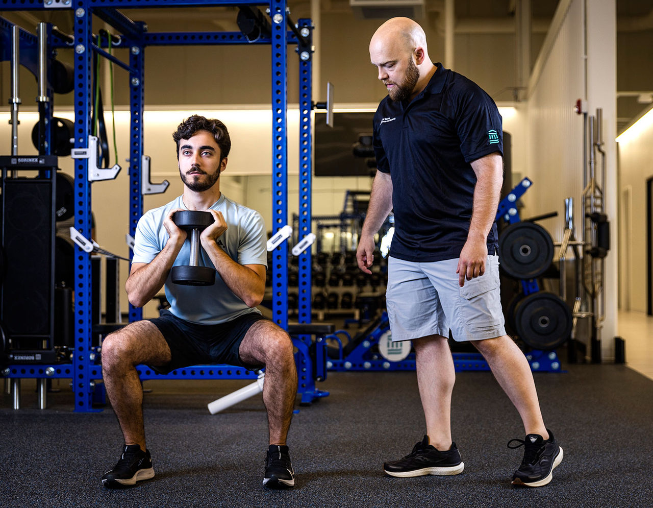 male trainer supervising a male athlete using a weight machine at gym