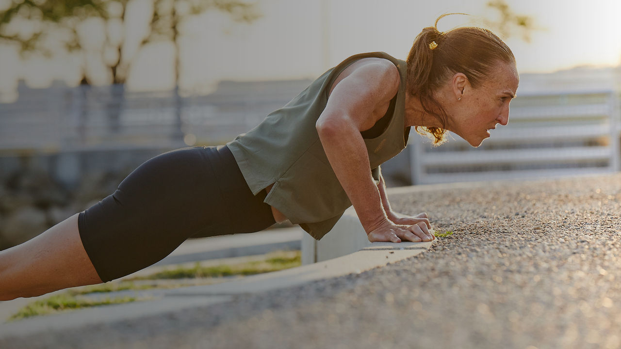 woman outdoors doing push-up against a concrete wall