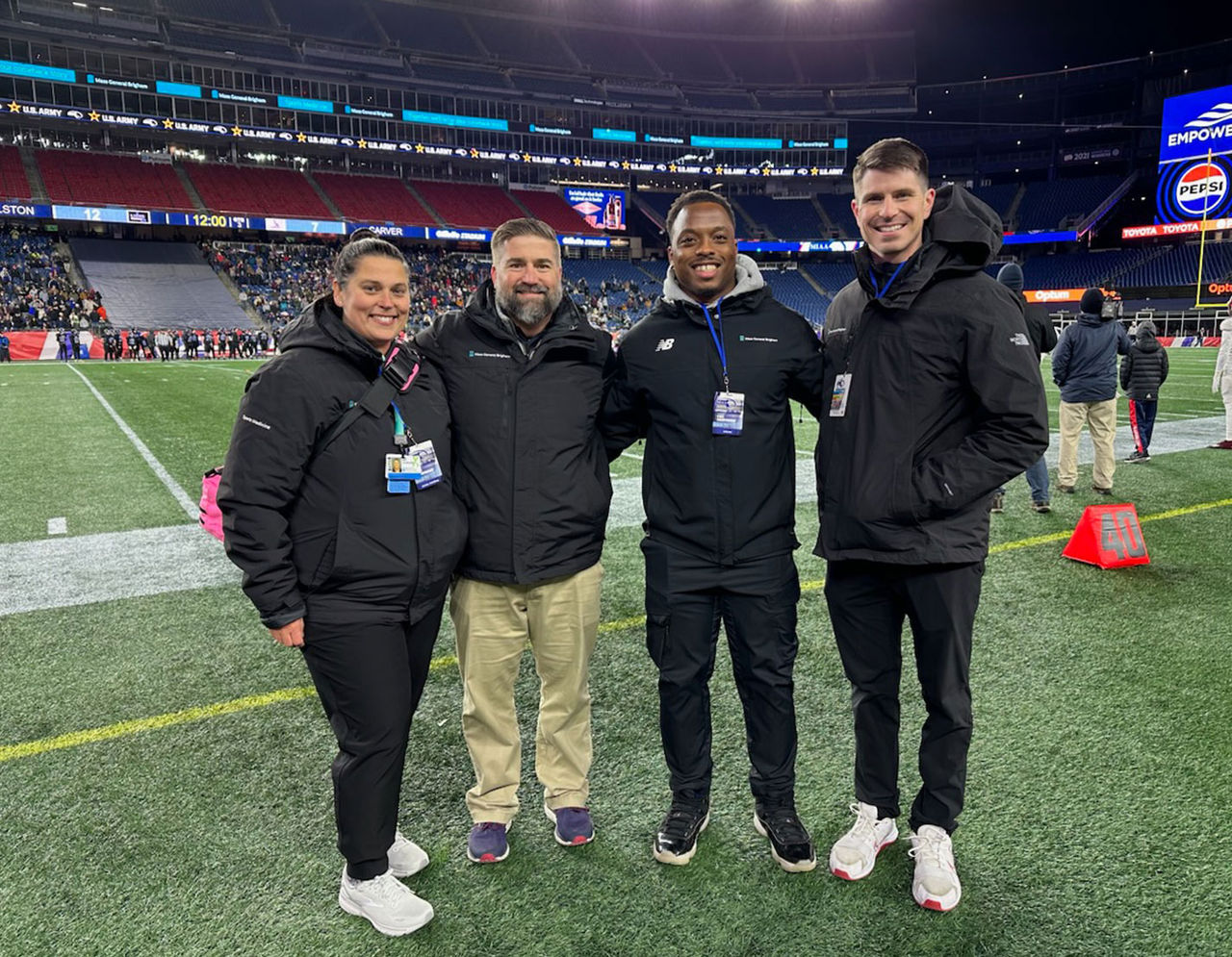 Four members of the Mass General Brigham Sports Medicine team standing together and smiling next to football field