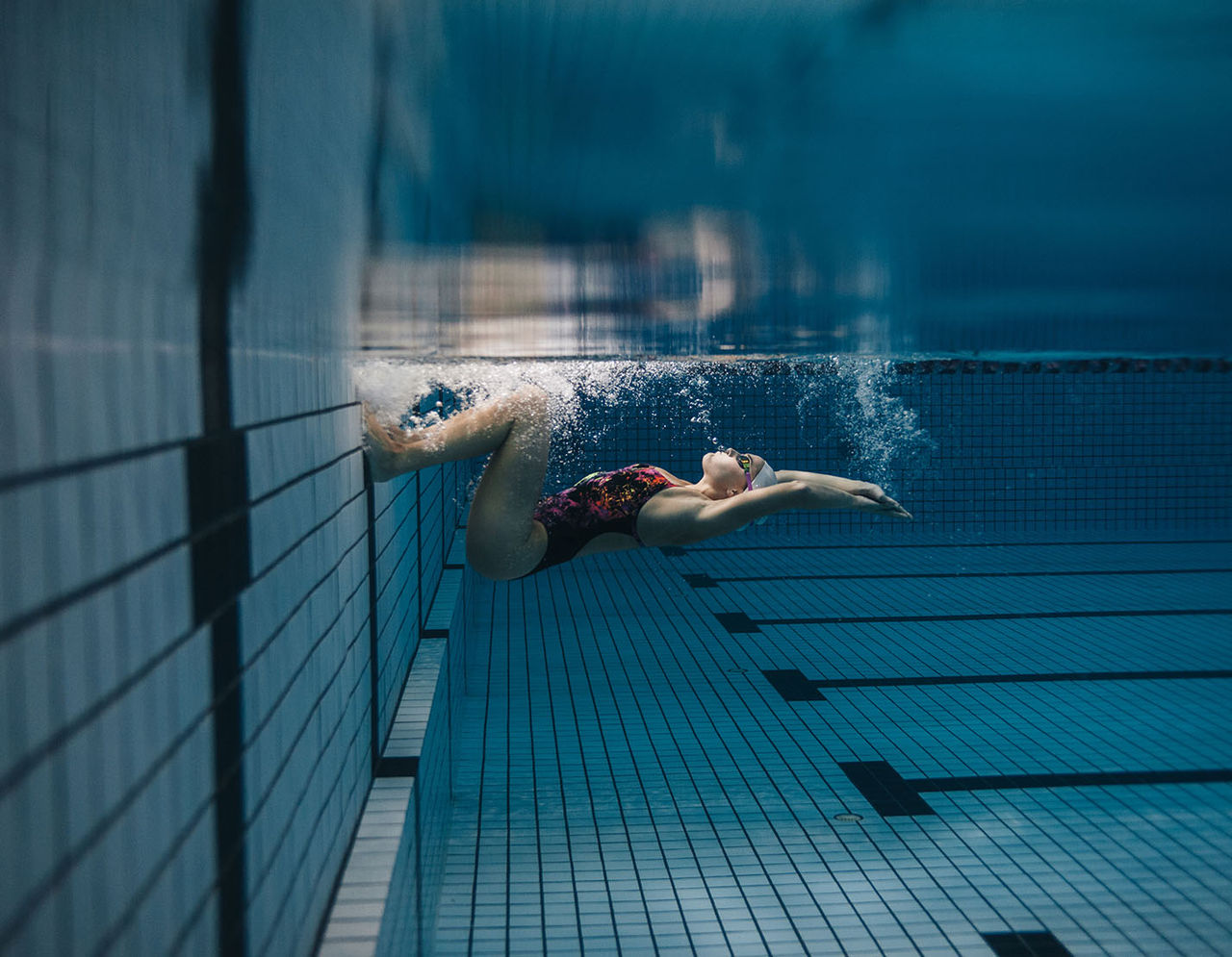 female swimmer in pool springing from wall