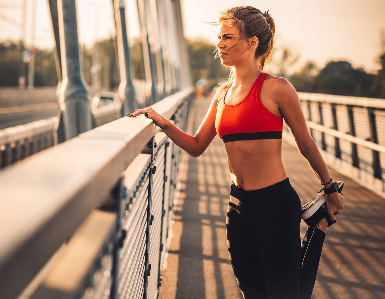 woman in running gear and sneakers stretching her leg holding onto a railing