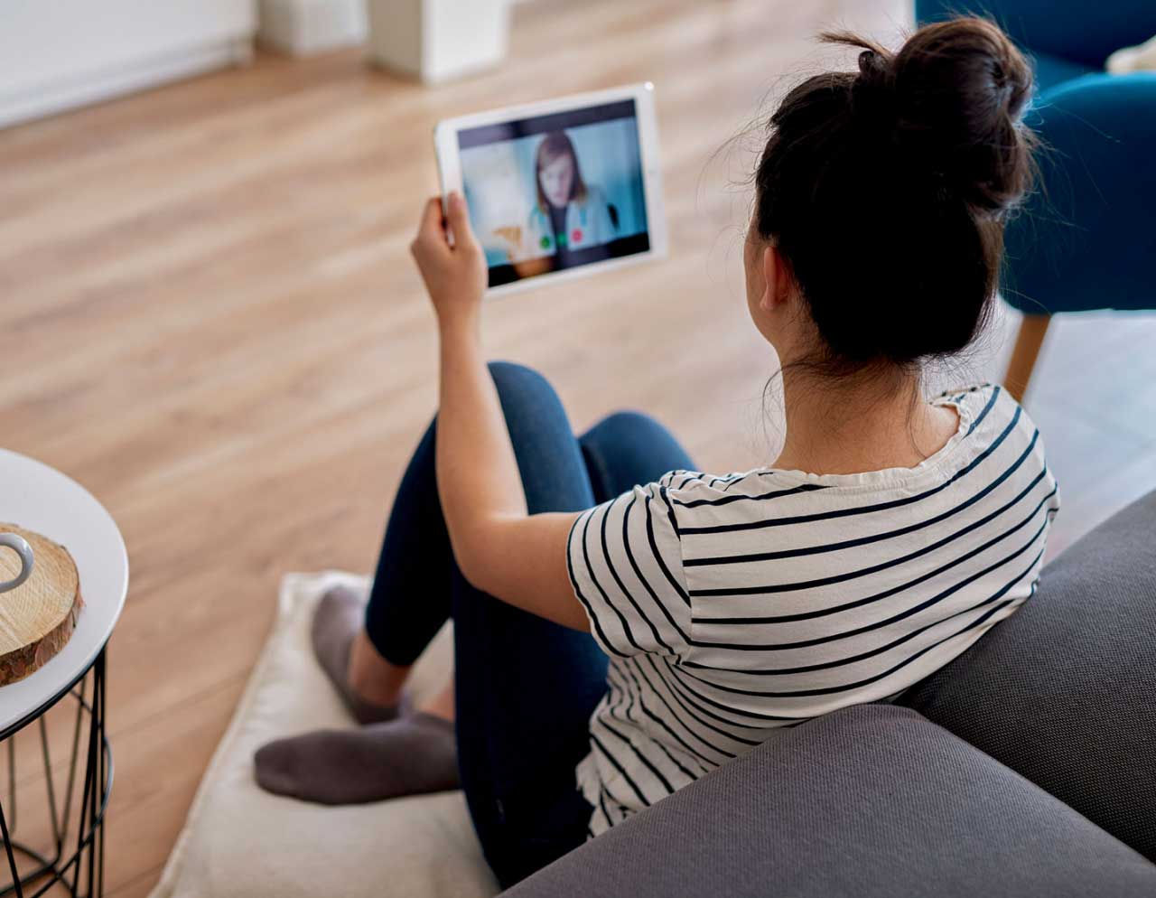 A woman talks to her doctor on a tablet from the comfort of her own living room.