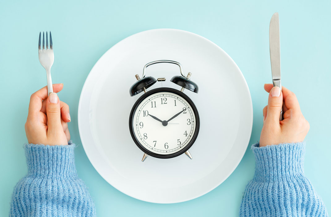 A clock on a dinner plate, with a woman's hands holding a fork and knife on either side.