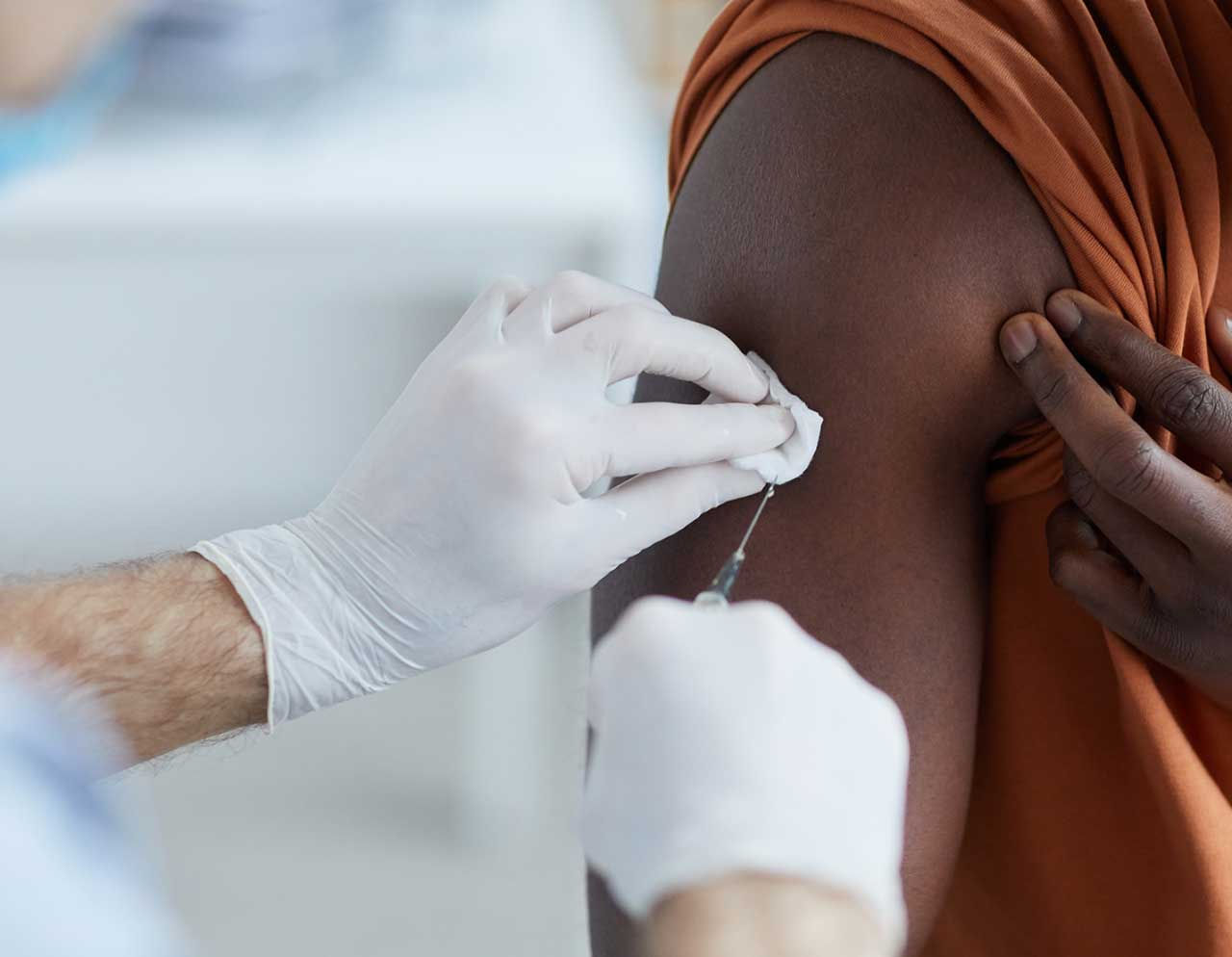 Man receiving a flu shot in his arm from clinician.