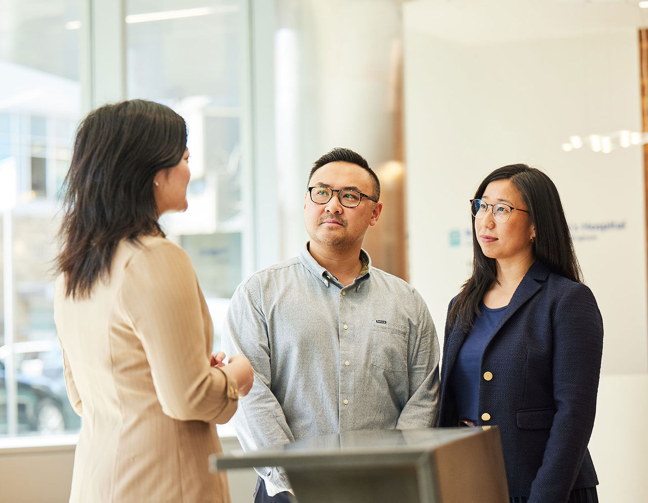 A Chinese couple speaks with a woman in a suit in the hospital lobby.