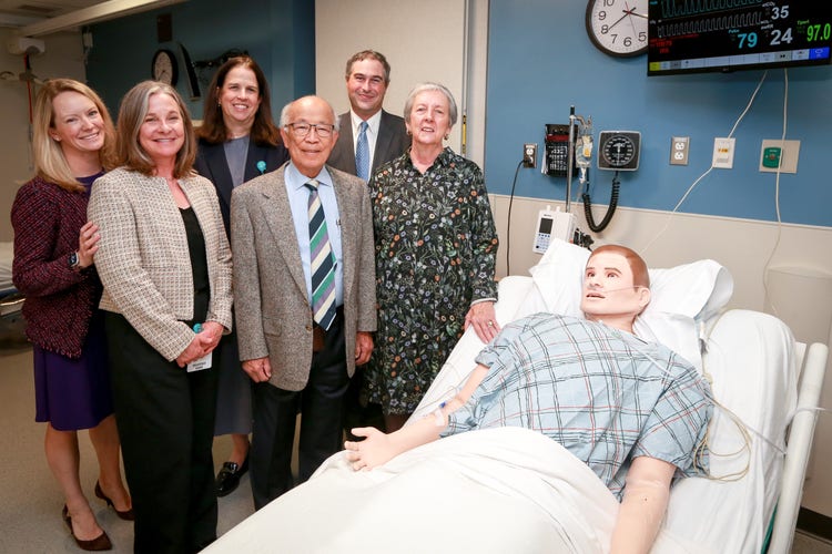 Nursing staff gathered at the bedside of a simulation lab with a mannequin in the bed.