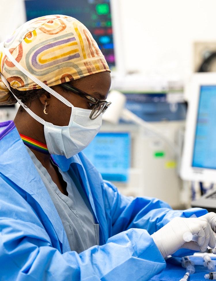 A healthcare professional in surgical scrubs and a colorful cap works at a medical station.