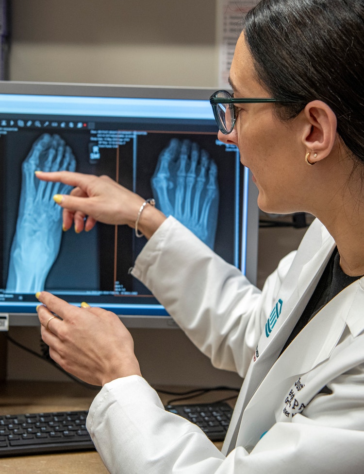 Doctor reviews foot X-ray images on computer monitor.