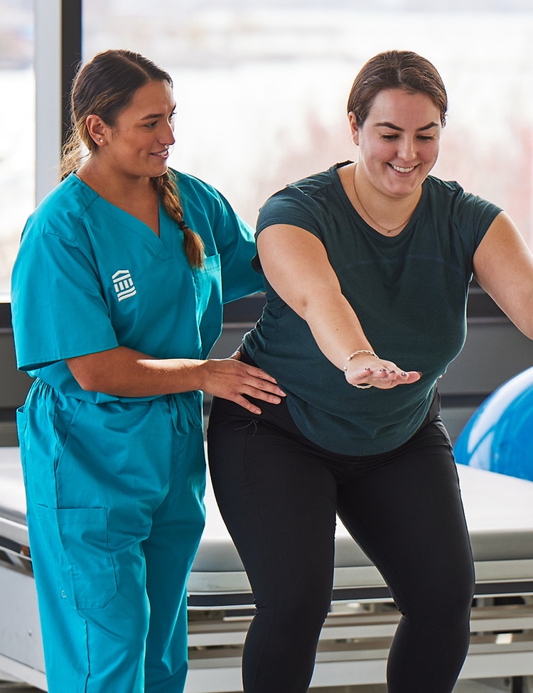A clinician assists woman with balance exercise.